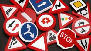 Zbiór różnorodnych szwajcarskich znaków drogowych, w tym znaki zakazu, nakazu, informacyjne i ostrzegawcze, ułożonych na czarnym tle, symbolizujących przepisy ruchu drogowego w Szwajcarii.